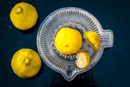 Raw fresh ripe lemons or Citrus Ã limon in a glass squeezer on black wooden surface in dark Gothic colors.の写真素材