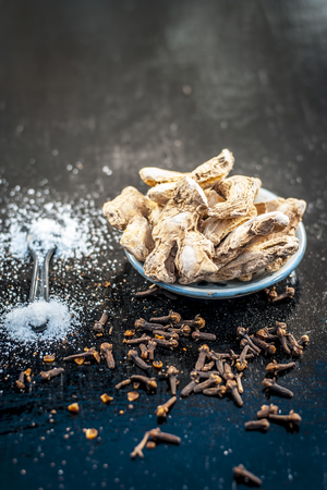 Close up of ayurvedic herb or folk medicine Dried Ginger or Zingiber officinale with black pepper corns and cloves on wooden surface with benefits like relieving nausea, loss of appetite etc.の写真素材