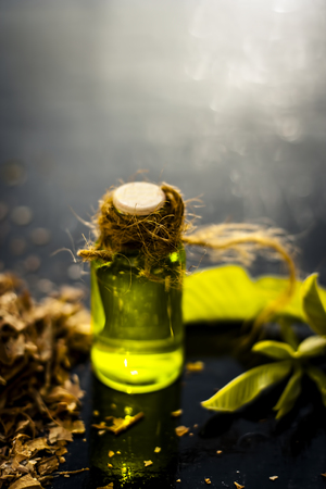 Close up of extracted beneficial oil of guava for weight loss, anti aging, and for god hair growth and for skin care with dried leaves of guava with fresh leaves in a bottle on wooden surface.の写真素材