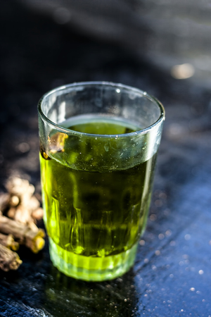 Herbal and beneficial extract or syrup of Indian sarsaparilla or Naruneendi or Nannari in a transparent glass on wooden surface with raw sarsaparilla.の写真素材