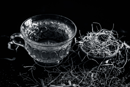 Beneficical Tea of Khus or Chrysopogon zizanioides or Vetiver grass in a transparent cup with raw dried vetiver grass on wooden surface.の写真素材