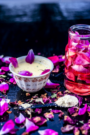 Close up of ayurvedic and beneficial face pack for dull and black skin i.e. Face pack of Rose water with gram flour and some rosa petals on wooden surface.の写真素材