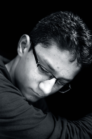 Portrait of a young teenager posing with a small smile on his face in a dark background wearing green hooded T-shirt.の写真素材