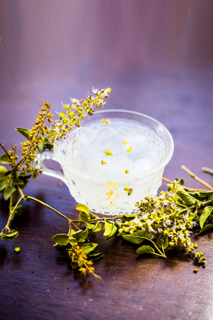White colored Ice tea in a transparent cup on brown colored wooden surface with some ice cubes and fresh bright leaves of holy basil.の写真素材