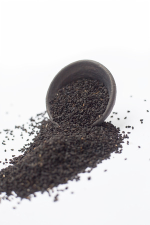 Kalonji or fennel flower dried seeds in a black colored clay bowl isolated on white.の写真素材