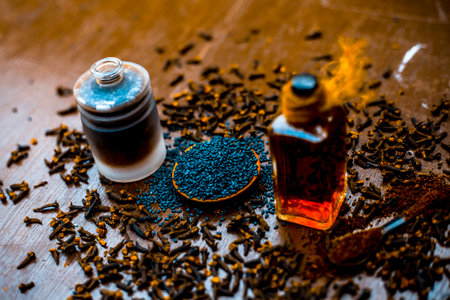 Close up of home remedy for earache i.e. Black sesame seeds oil with clove oil. Raw black sesame seeds and cloves on wooden surface.の写真素材