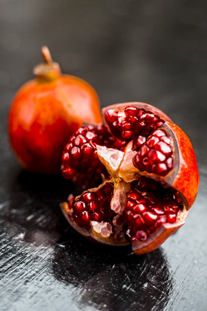Close up of raw red colored ripe pomegranate with cut pomegranate on wooden surface with some rose leaves.の写真素材