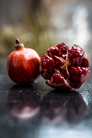 Close up of raw red colored ripe pomegranate with cut pomegranate on wooden surface with some rose leaves.の写真素材