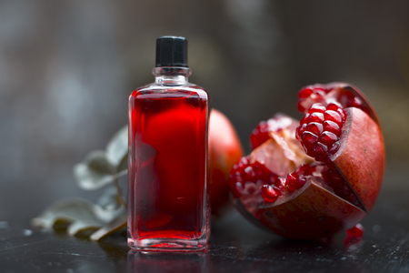 Close up of essential oil of pomegranate with raw ripe pomegranate on wooden surface in transparent bottle.の写真素材