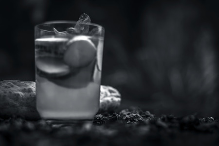 Close up of fresh cucumber water in a glass on wooden surface with some sliced lemons and cucumber in it and some ice cubes.の写真素材