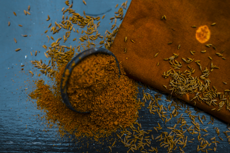 Close up of powdered cumin or zeera or jeera with raw cumin on wooden surface in a clay bowl on a cloth or napkin.の写真素材