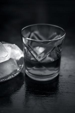 Close up of Scotch whiskey or Grain scotch in a transparent glass with ice cubes on black colored wooden surface.の写真素材