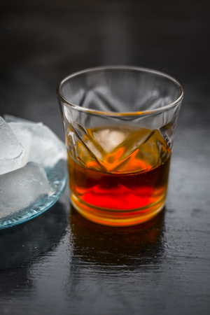 Close up of Scotch whiskey or Grain scotch in a transparent glass with ice cubes on black colored wooden surface.の写真素材