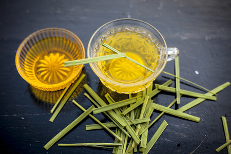 Close up of Iced lemon grass tea in a transparent cup on wooden surface with raw lemon grass green tea in a cup and sugar in a clay bowl with ice cubes in the cup and a piece of ginger and honey.の写真素材