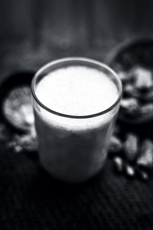 Close up of kharek or dried dates with raw milk in a transparent glass on brown colored surface with some powder of dried dates in a black colored clay bowl.の写真素材