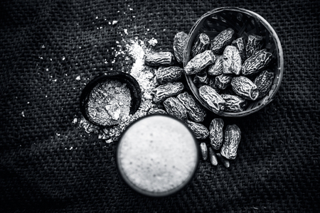 Close up of kharek or dried dates with raw milk in a transparent glass on brown colored surface with some powder of dried dates in a black colored clay bowl.の写真素材