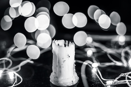 Close up of white colored half burned exhausted wax candle on wooden surface with blurred background or bokeh of colorful lights of Christmas with it.の写真素材