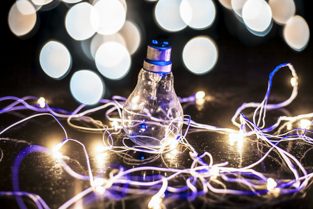 Close up of a bulb on wooden surface with colorful blurred background or bokeh of Christmas lights with it.の写真素材