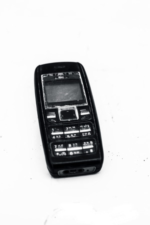 Close up of a black colored old cell phone with black colored body and broken switches and screen isolated on white.の写真素材