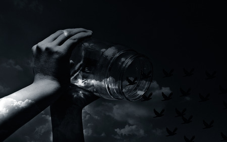 Close up of human hands holding a glass bottle and letting birds fly away with sky background and a sun flair on it.の写真素材