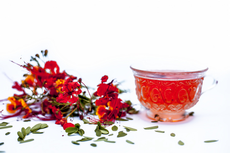 Close up shot of herbal organic fresh tea of peacock flowers in a transparent  glass cup with flowers isolated on white.