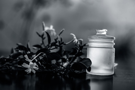 Close up shot of extracted essential oil of Indian jasmine flower in a transparent glass bottle on wooden surface with raw jasmine flowers.の写真素材