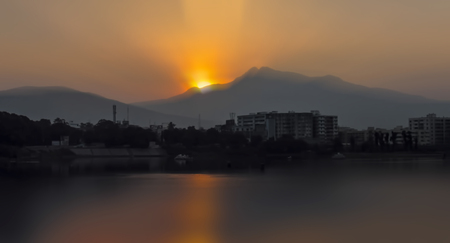 Landscape of mountains and lake during dawn time in the morning sun rising behind the clouds and Tyndall effect on water.の写真素材