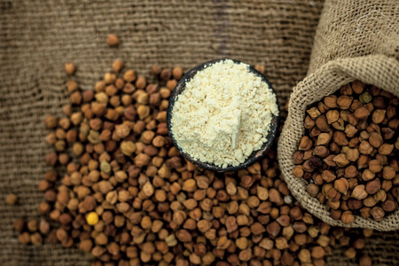 Close up of a jut bag full of chickpeas or grams in it and its floor or besan ka atta in a clay bowl on brown colored surface.の写真素材