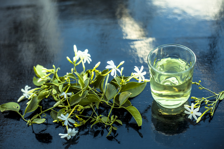 Close up of extract of Indian jasmine flower or juhi or Jasminum Auriculatum on wooden surface in a transparent glass with raw flowers.の写真素材
