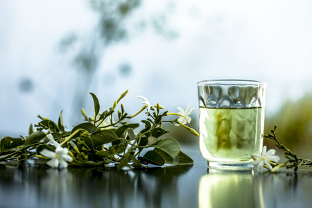 Close up of extract of Indian jasmine flower or juhi or Jasminum Auriculatum on wooden surface in a transparent glass with raw flowers.の写真素材