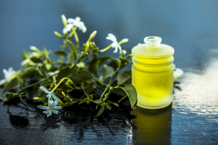 Close up shot of extracted essential oil of Indian jasmine flower in a transparent glass bottle on wooden surface with raw jasmine flowers.の写真素材