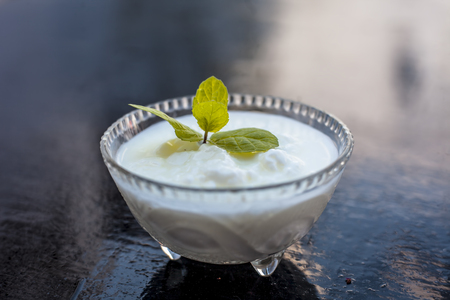Close up of raw organic curd in a glass bowl along with mint leaf on the top for decoration on wooden surface.の写真素材