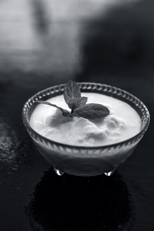 Close up of raw organic curd in a glass bowl along with mint leaf on the top for decoration on wooden surface.の写真素材