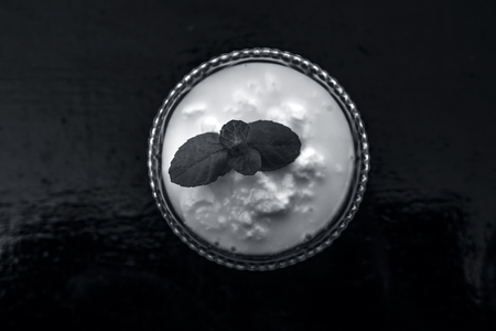 Close up of raw organic curd in a glass bowl along with mint leaf on the top for decoration on wooden surface.の写真素材