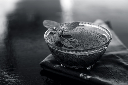 Close up of soaked sabja seeds or falooda seeds or sweet basil seeds in a glass bowl on brown colored napkin on wooden surface with some mint leaves in it.Used in many flavored beverages.の写真素材