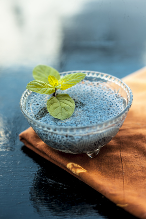 Close up of soaked sabja seeds or falooda seeds or sweet basil seeds in a glass bowl on brown colored napkin on wooden surface with some mint leaves in it.Used in many flavored beverages.の写真素材