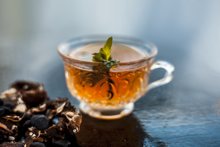 Tamarind or imli or amli in a clay bowl along with its roasted seeds and extract tea in a transparent glass cup with mint or mentha leaves on top on wooden surface.の写真素材