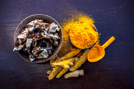 Tamarind or imli or amli in a clay bowl along with its roasted seeds on wooden surface with turmeric or haldi in a clay bowl used for treating acne and pimple.の写真素材
