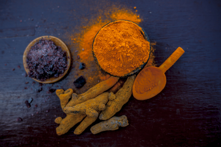 Close up of clay bowl full of turmeric powder along with some raw turmeric and black salt in another bowls on shiny surface.の写真素材