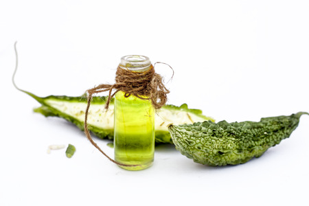 Raw organic bitter melon or Bitter Cucumber or Bitter Gourd isolated on white along with its detoxifying essential oil in a transparent glass bottle.の写真素材