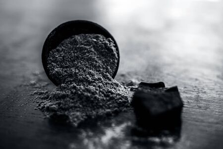 Raw organic hing or devil's dung or Asafoetida on wooden surface along with its powder in a black colored clay bowl and some mint leaves or mentha leaves on it.の写真素材