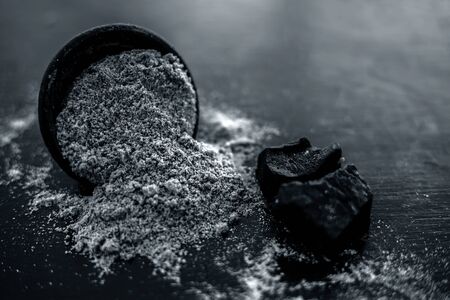 Raw organic hing or devil's dung or Asafoetida on wooden surface along with its powder in a black colored clay bowl and some mint leaves or mentha leaves on it.の写真素材
