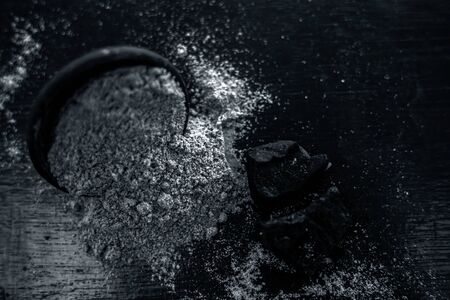 Raw organic hing or devil's dung or Asafoetida on wooden surface along with its powder in a black colored clay bowl and some mint leaves or mentha leaves on it.の写真素材