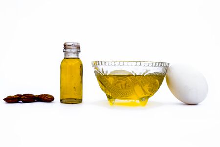 Home remedy to cure hair damage isolated on white i.e. almond oil along with egg white well mixed in a glass bowl and all the raw ingredients present on the surface.の写真素材