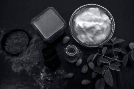 Organic hair conditioner on wooden surface i.e. Hing or devil's dung and almond oil with yogurt in a glass bowl and all the raw ingredients present on the surface with some rose leaves.の写真素材