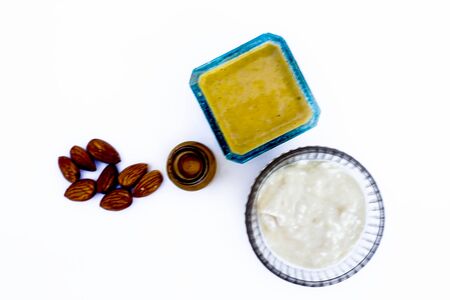 Hair conditioner isolated on white i.e. Almond oil well mixed with yogurt or curd in a blue colored glass bowl and entire ingredients present on the surface including raw almonds.の写真素材