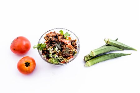 Popular Indian Lunch dish isolated on white i.e. Bhareli Bhindi or bareli bindi or fried crispy stuffed okra,with raw okra pods and tomatoes.の写真素材
