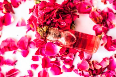 Rose petals spread on the surface along with a small glass bottle of essential rose concentration or...