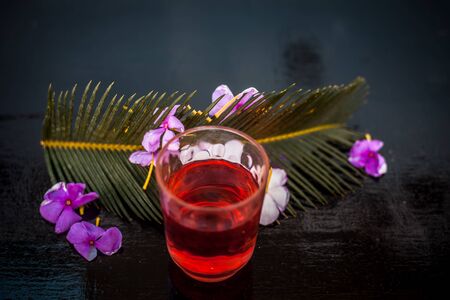 Extracted tincture or extraction of rosemary flower in a glass on wooden surface along with rosemary flowers and leaves.の写真素材