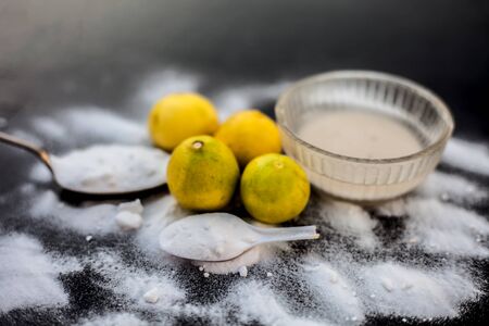 Baking soda face mask in a glass bowl on wooden surface along with some baking soda sprinkled on the surface and lemons also on surface. Used to blemishes skin instantly.の写真素材